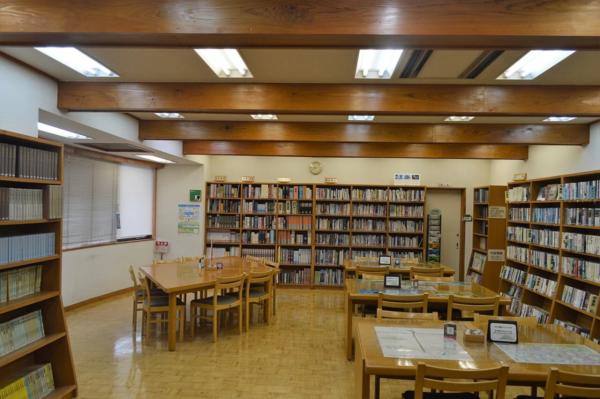 An empty library reading room with wooden tables, chairs and tall shelves of books