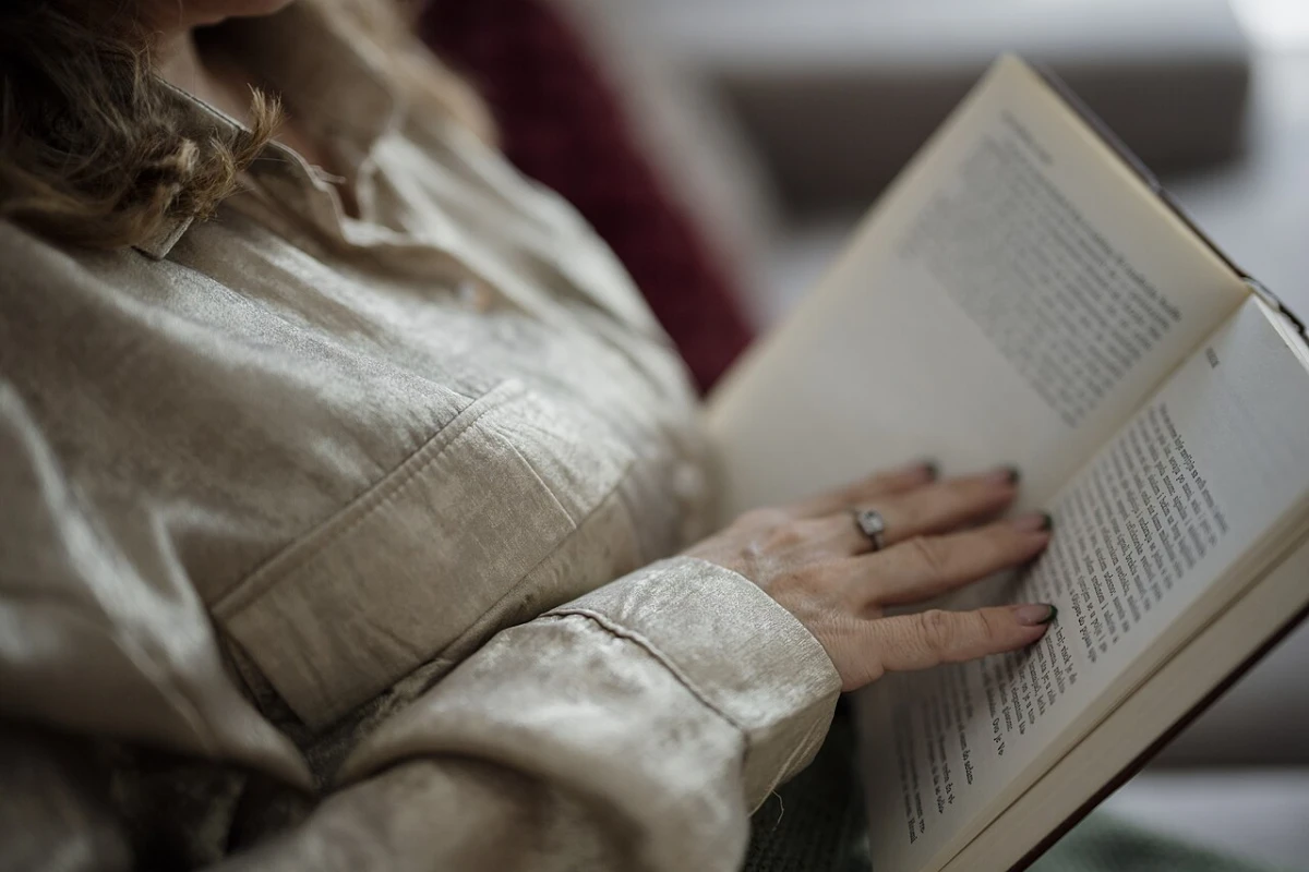 A reader holds an open paperback with one hand resting on the page